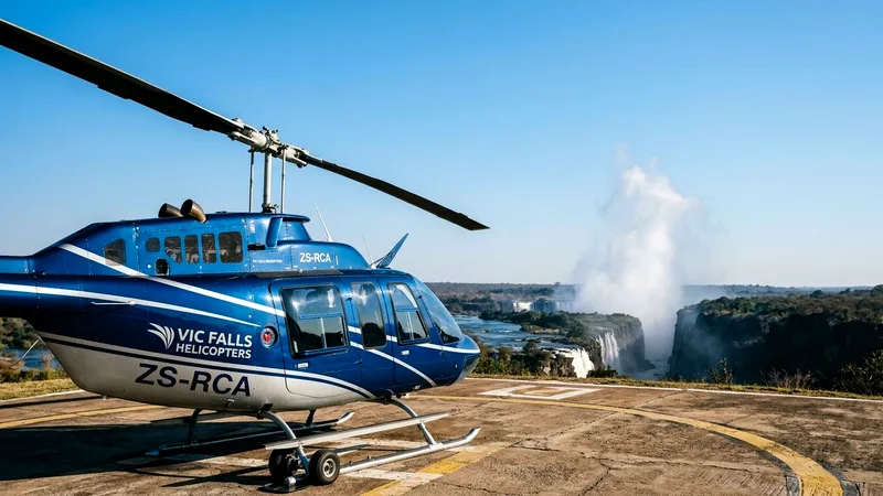 Blue helicopter on a landing pad with Victoria Falls spray in the distance